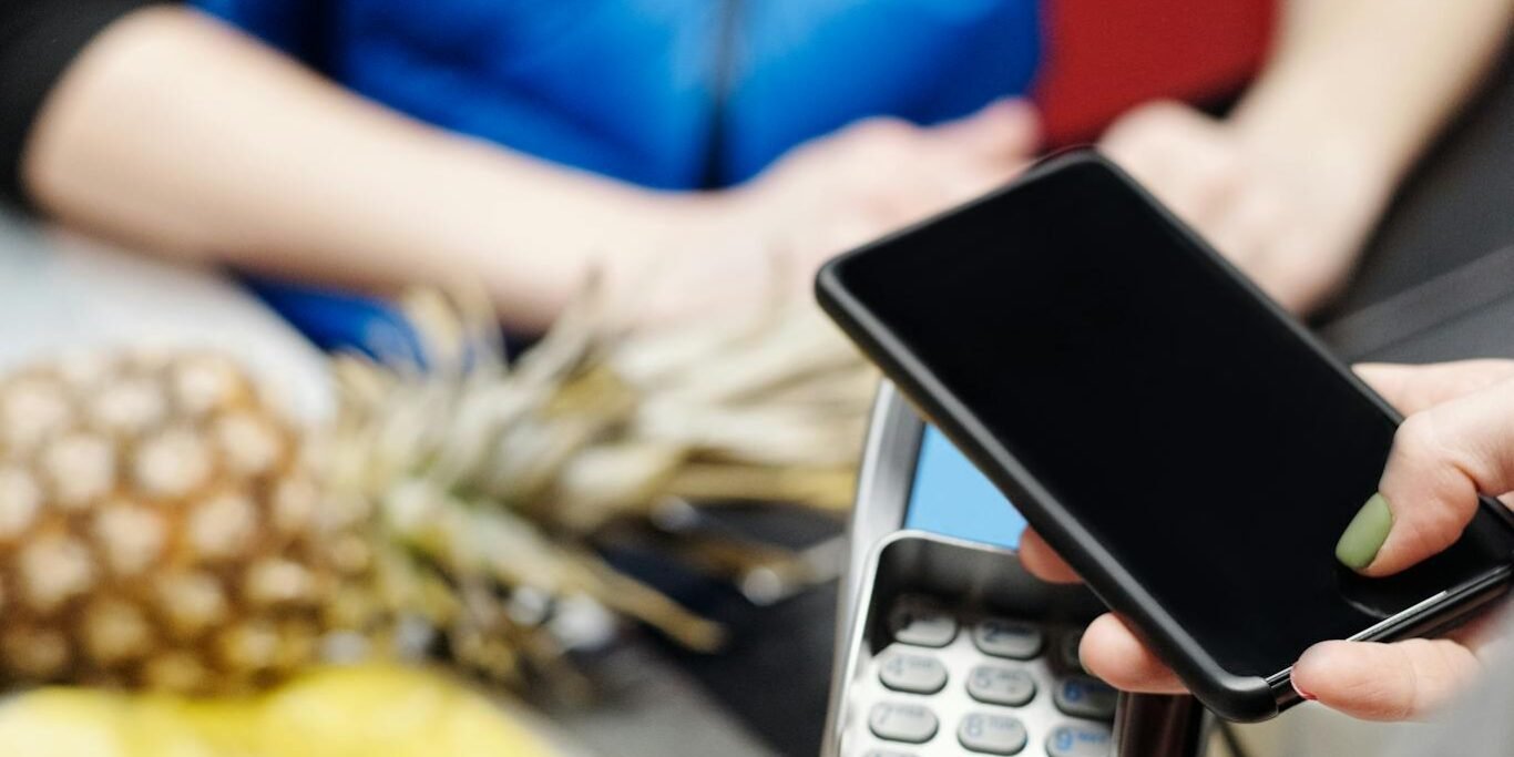 Photo by Jack Sparrow A customer uses a smartphone for contactless payment at a retail checkout with fresh produce.
