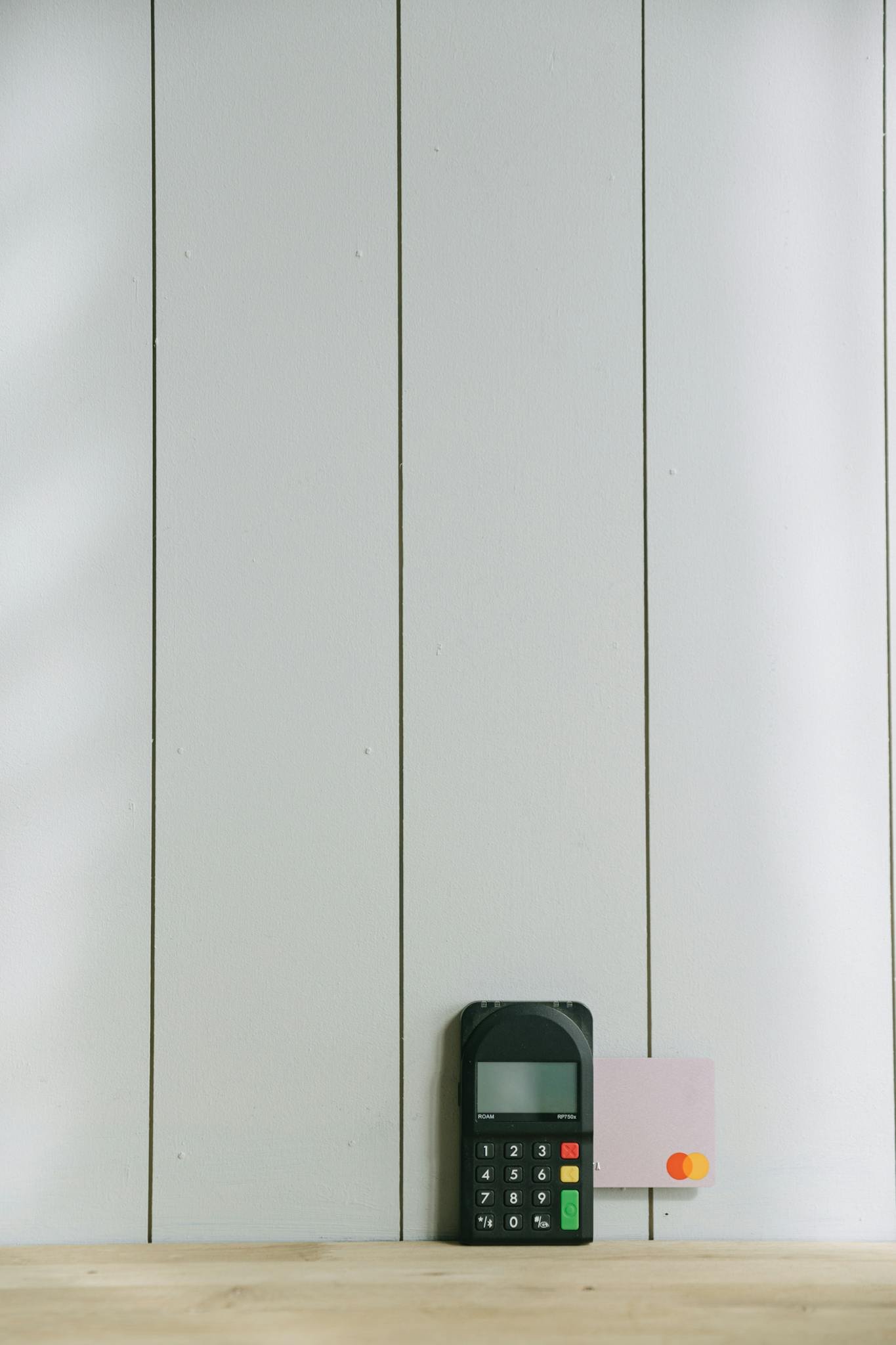 Photo by Ivan Samkov A sleek payment terminal with buttons against a white wooden background, ideal for finance concept.