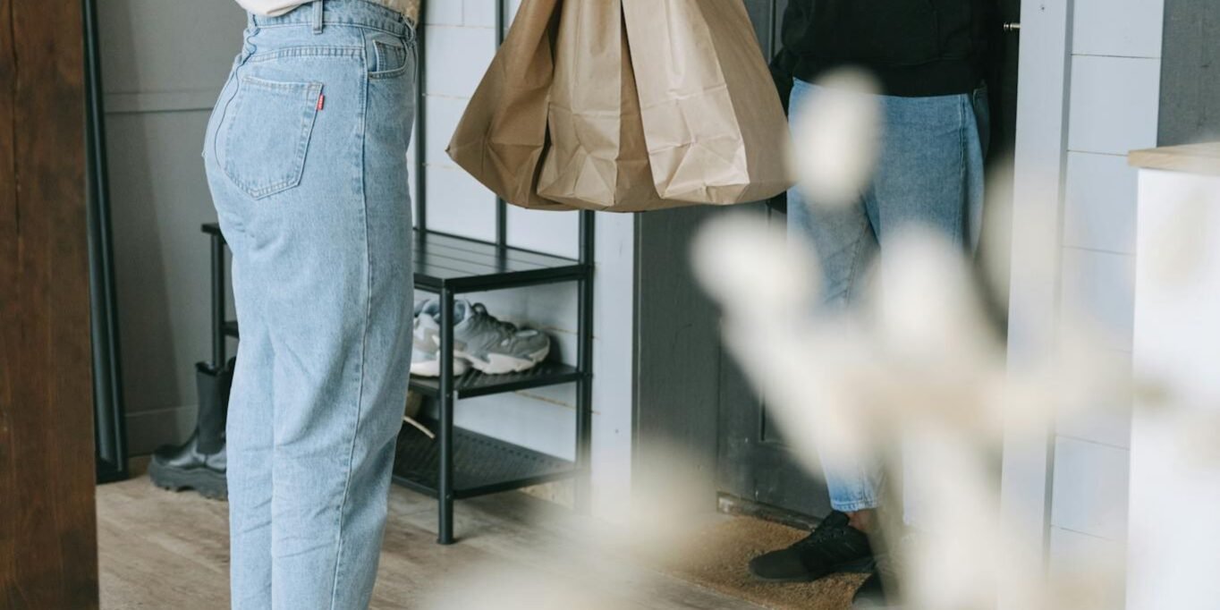 Photo by Ivan Samkov A woman receives a delivery package from a courier at her doorstep inside a modern home.