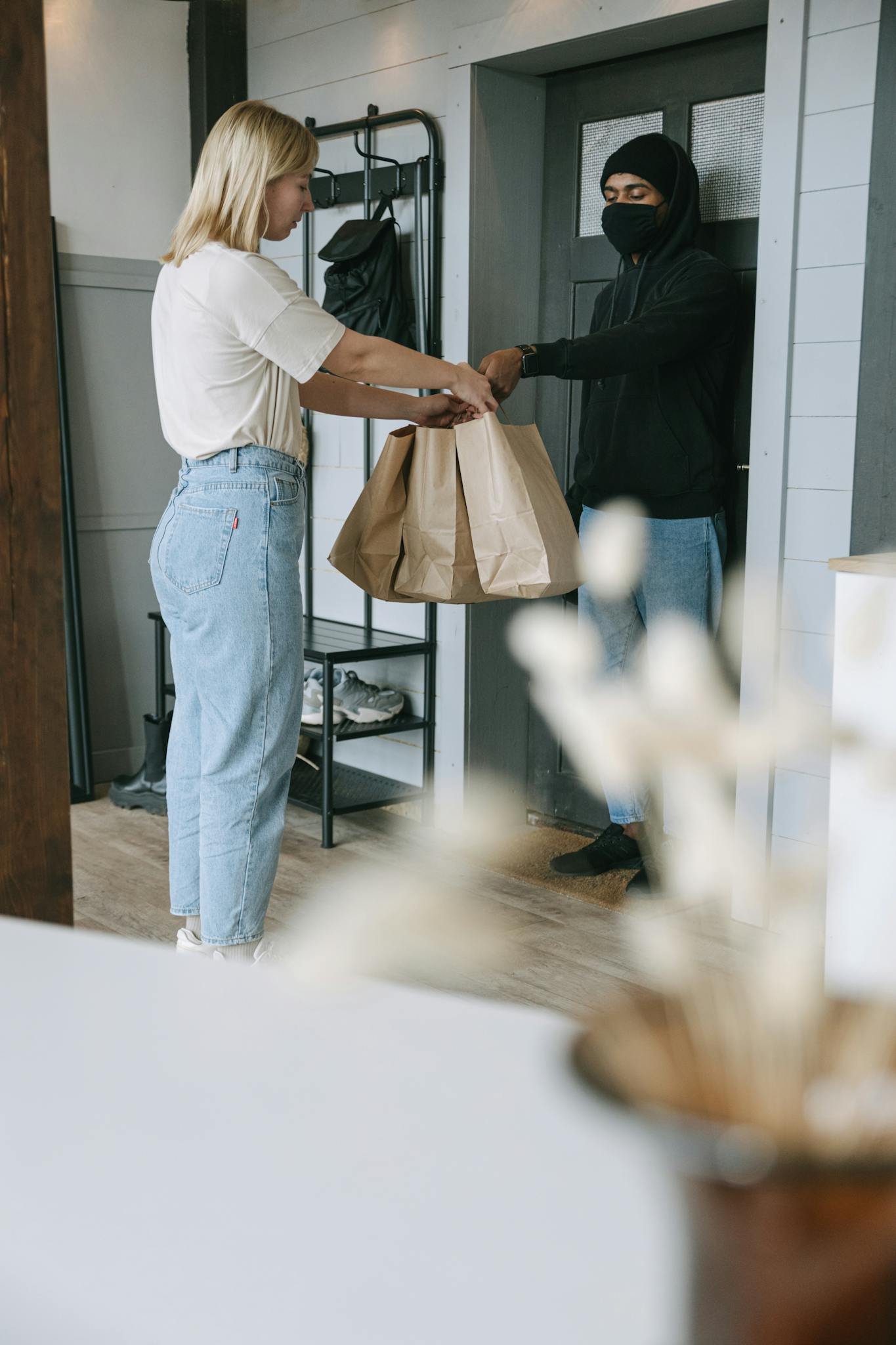 Photo by Ivan Samkov A woman receives a delivery package from a courier at her doorstep inside a modern home.