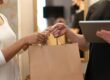 Close-up of hands exchanging a shopping bag indoors, symbolizing modern retail and technology.