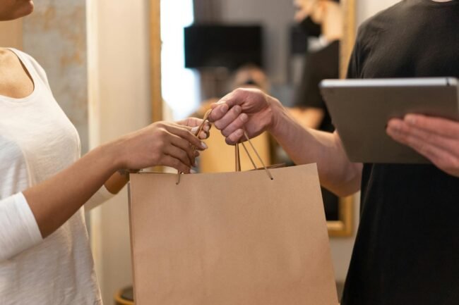 Photo by Mikhail Nilov Close-up of hands exchanging a shopping bag indoors, symbolizing modern retail and technology.